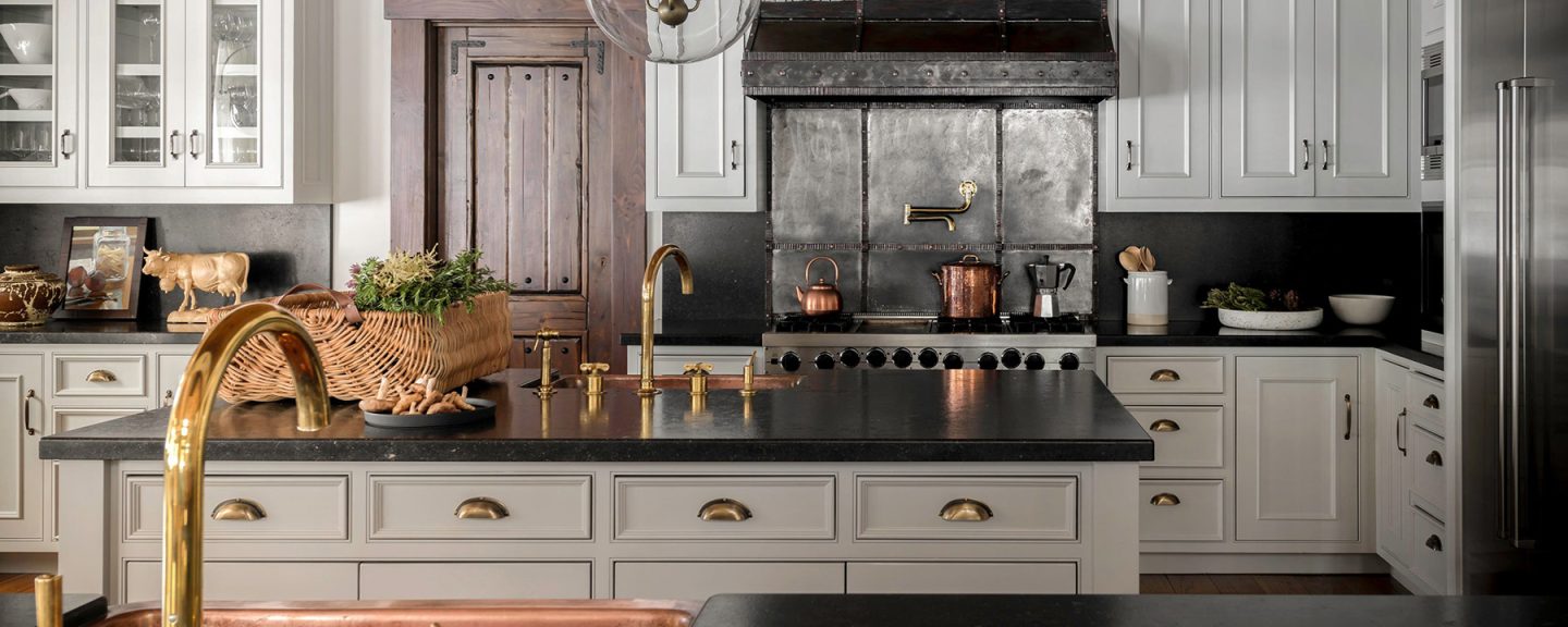 Close-up of unlacquered brass kitchen cabinet hardware and gold pot filler faucet over professional range